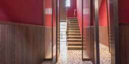 Boiserie moderna in noce canaletto cannettato nell'ingresso di una residenza a Faenza, con scala e pareti rosse
